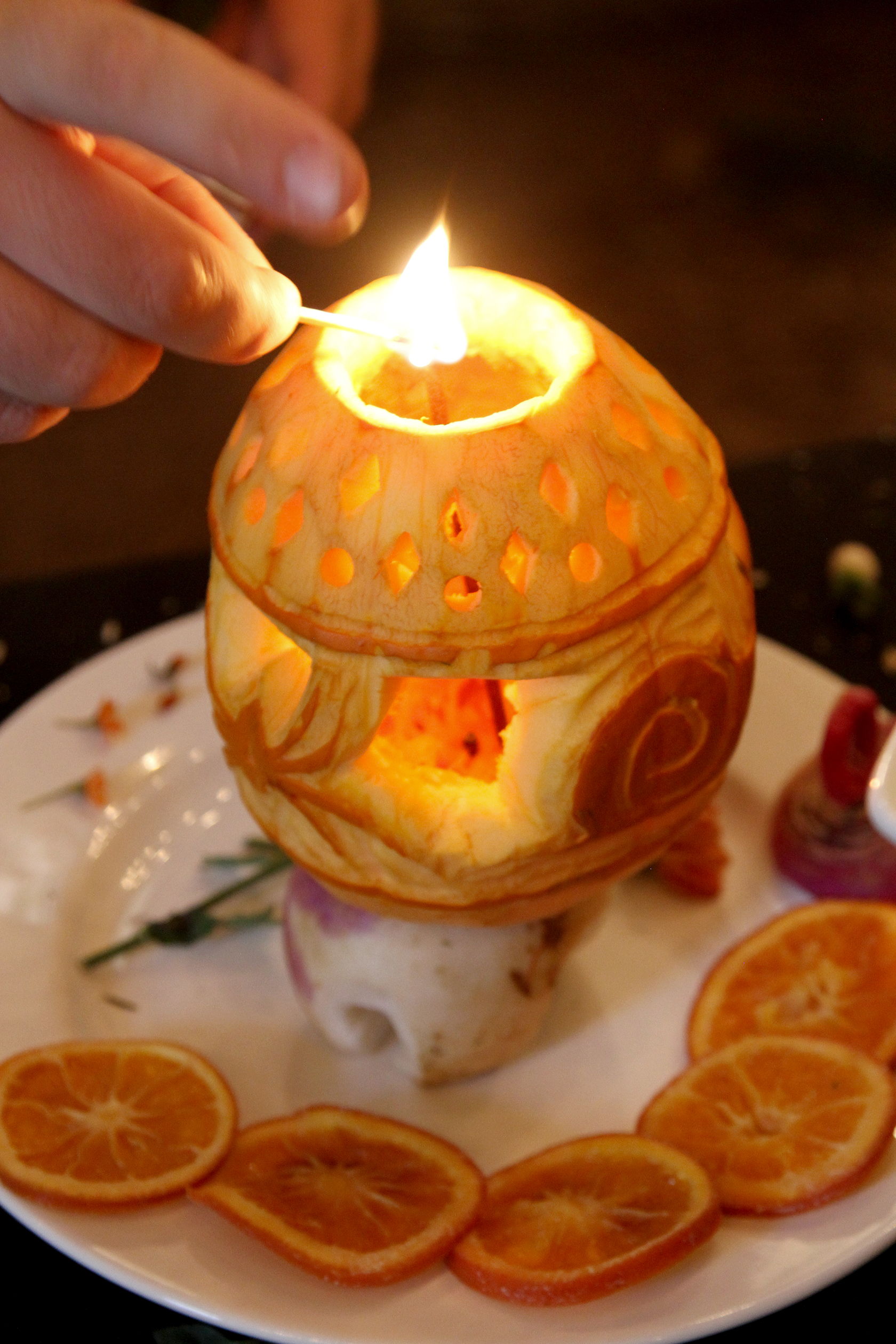 Image of a hand lighting an incense in a lantern made out of pumpkin on a white plate